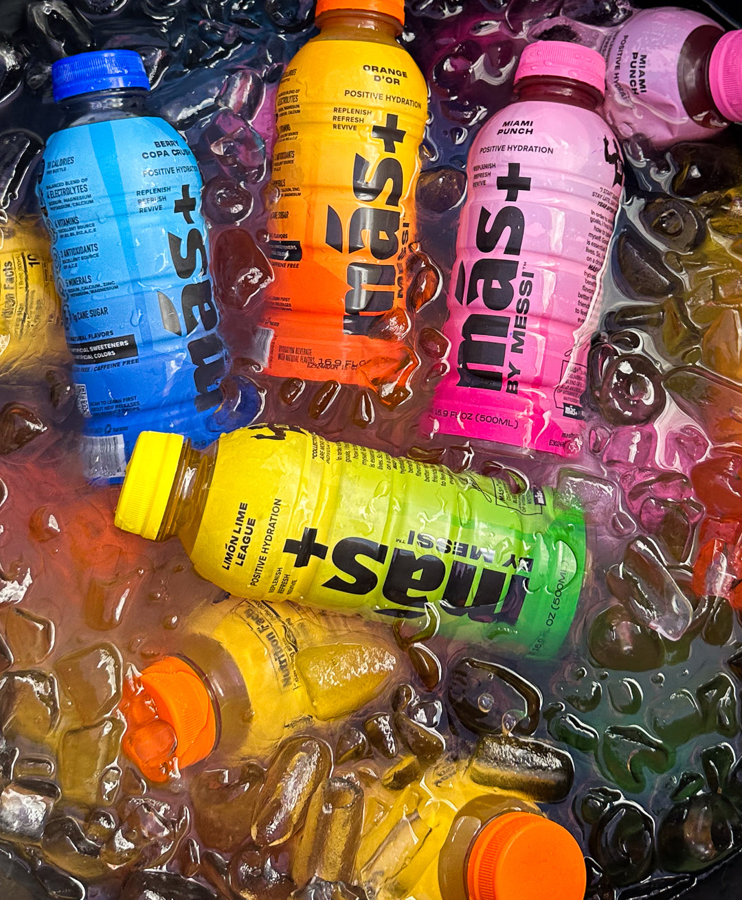 Assorted bottles of colorful hydrating drinks in ice, branded as Más+ by Messi. The drinks vary in color, including blue, orange, yellow and pink.