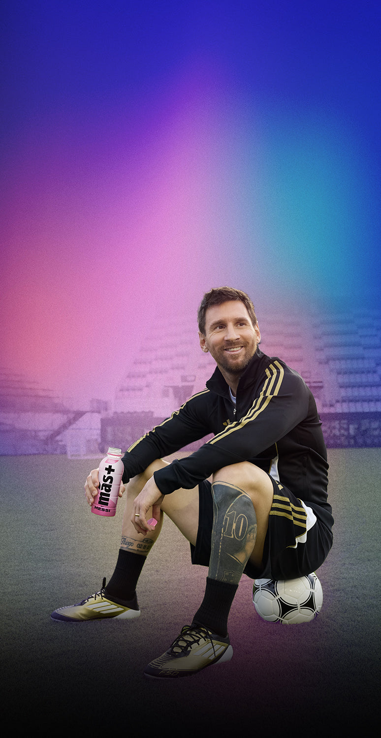 An image of Messi sitting on a soccer ball on a field. He is wearing a black and gold tracksuit with matching cleats and has a tattoo on his left leg. He is smiling and holding a pink and white sports drink bottle in his right hand. The background consists of blurred stadium stands with a gradient of purple, blue, and pink colors overlaying the image.