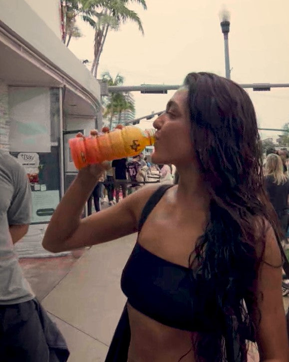 A person in a bikini drinks from an orange Más+ by Messi bottle.